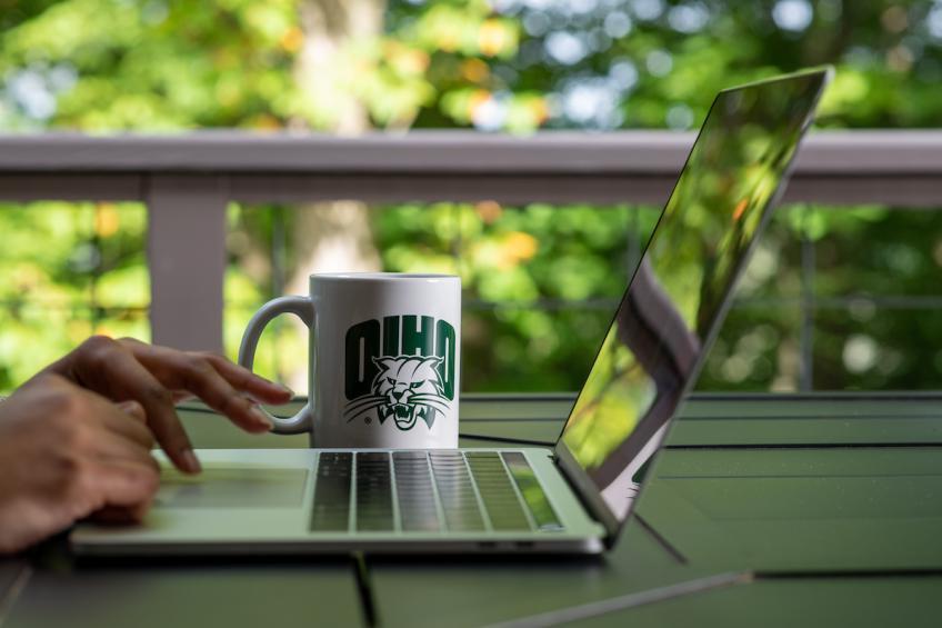 A student works on a laptop computer with an OHIO mug in the background.